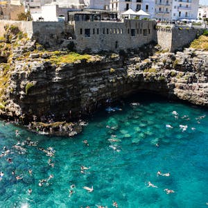 Beautiful seaside view of Polignano a Mare with swimmers in crystal-clear water.