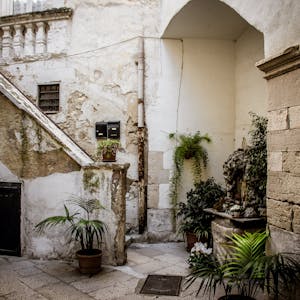 Explore a beautiful rustic courtyard in Apulia, Italy, featuring stone architecture and lush potted plants.